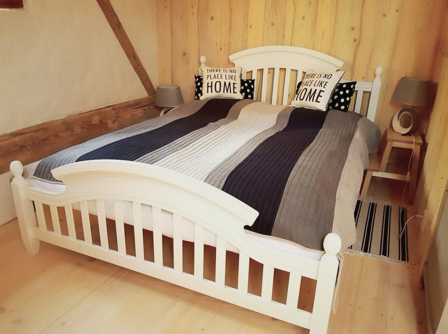Bílá postel s pruhovaným přehozem pod šikmým stropem